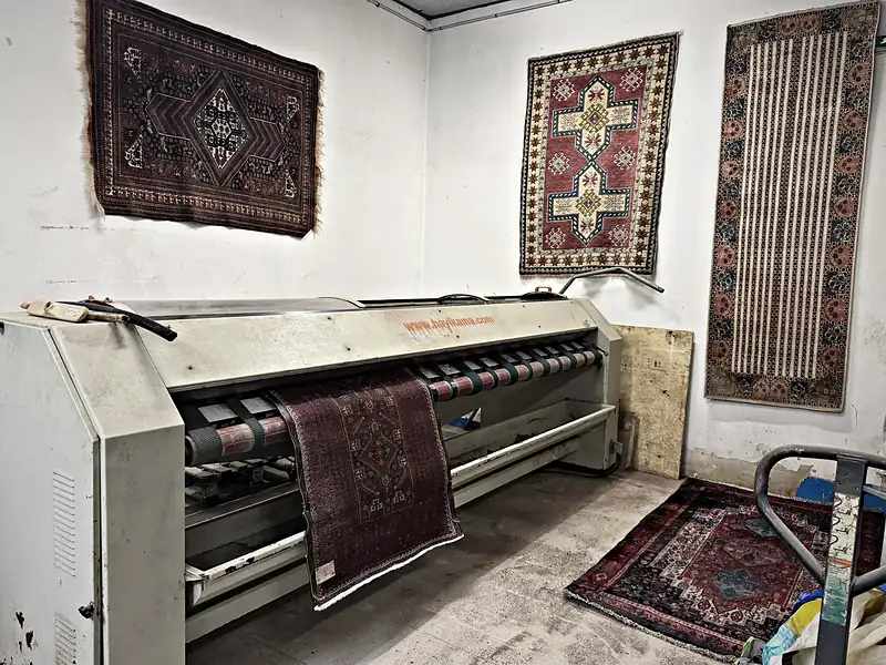 Salle de dépoussiérage de l’atelier, tapis anciens au mur.