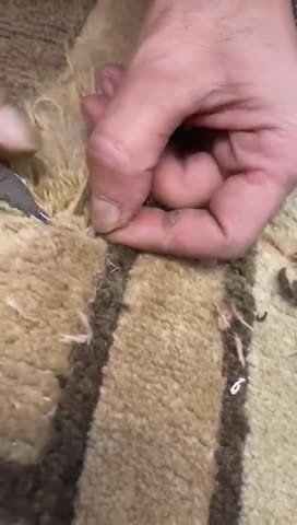Mains d’un artisan reprenant à l’aiguille la trame d’un tapis ancien.
